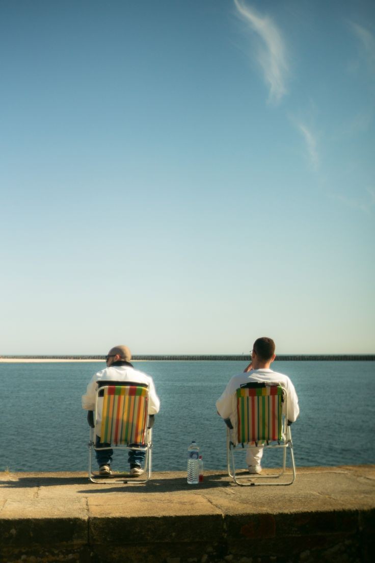 Two friends sitting in striped folding chairs, looking out at the sea
